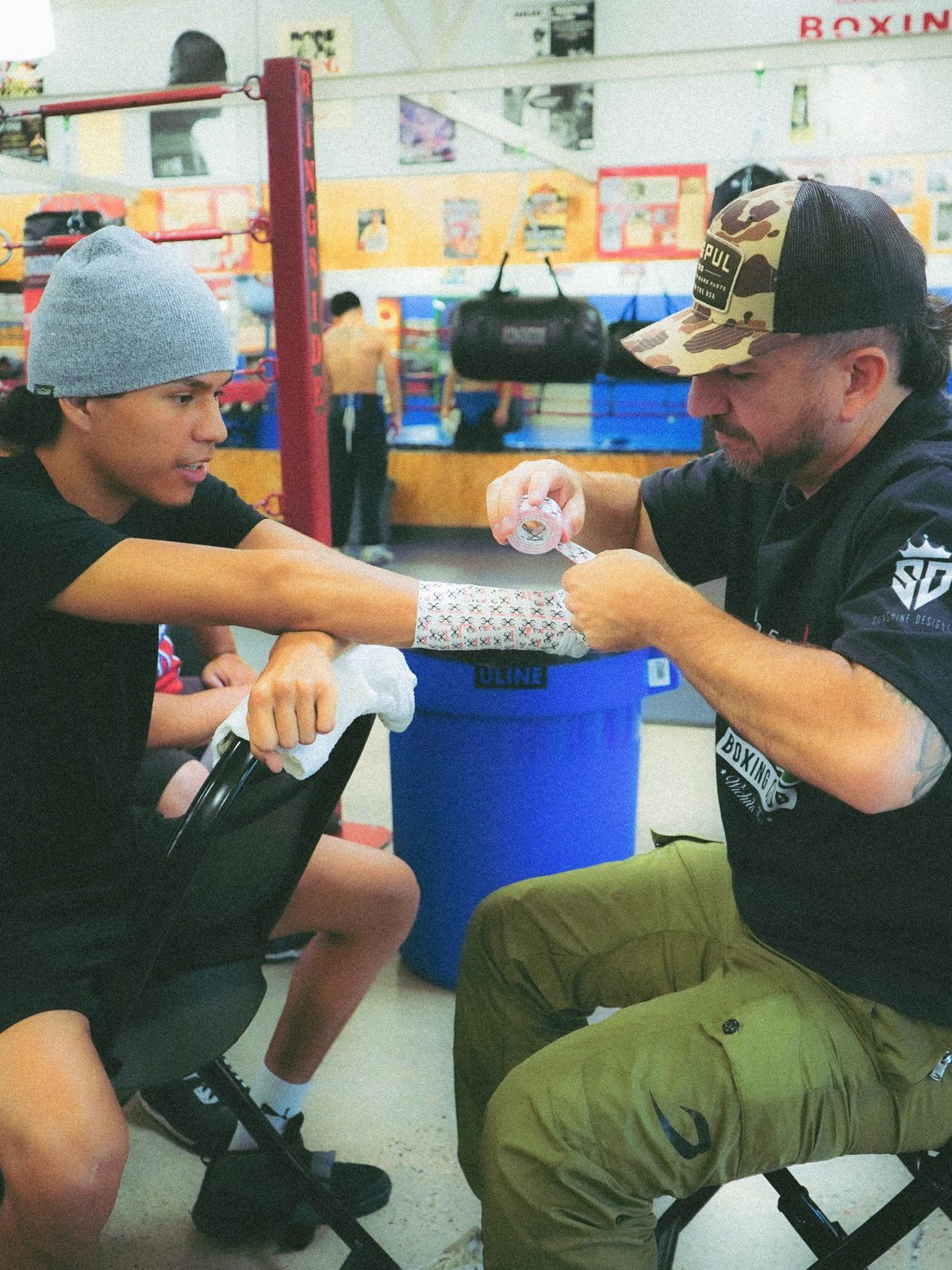 Coach Paco wrapping an athlete’s hands beside the ring. Public Instagram photo by @callfrank47.